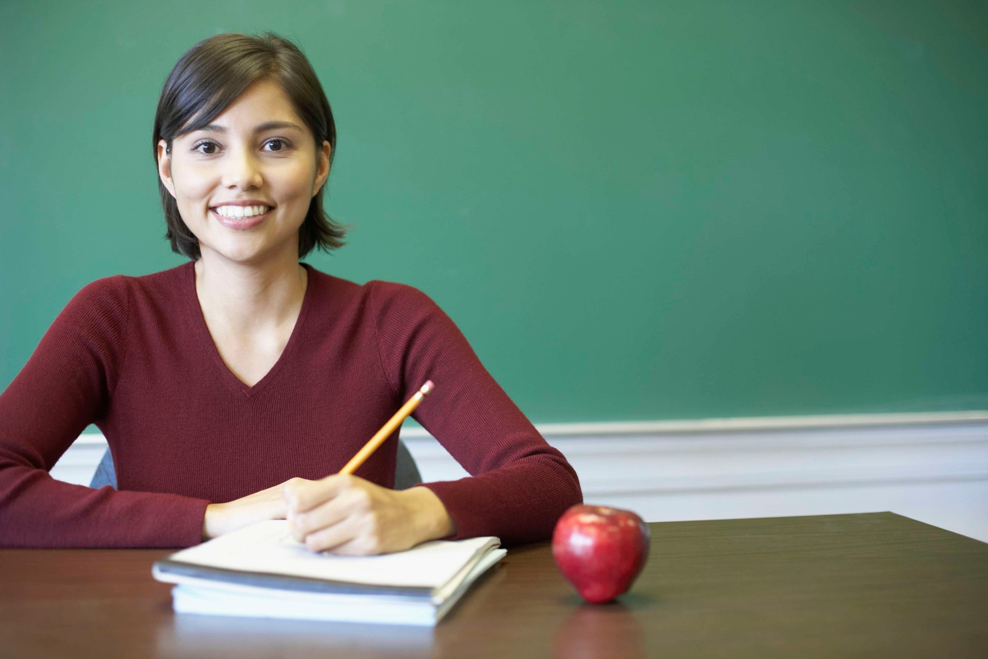 Smiling teacher in front of green chalkboard